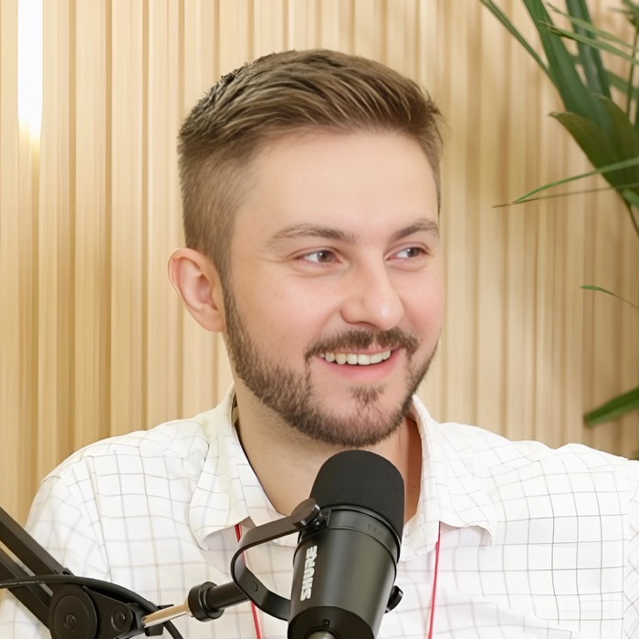 Eduardo Sebastiany sorrindo, de camisa quadriculada, diante de um microfone de estúdio